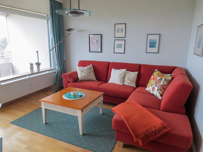 Wohnbereich mit rotem Ecksofa, Couchtisch und Fenster zum Balkon