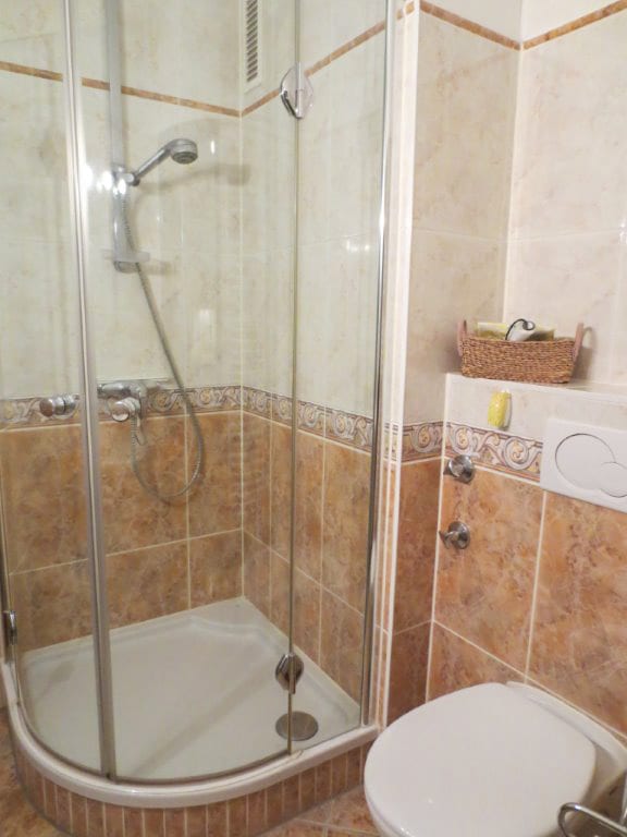 Badezimmer mit Eckduschkabine, Handbrause, WC und Handtuchkorb auf der Ablage