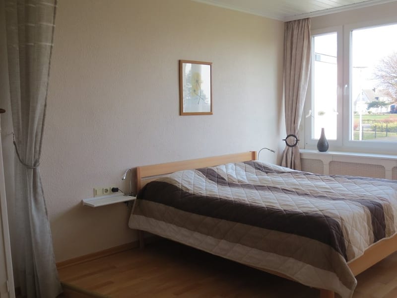 Schlafzimmer mit Doppelbett aus Holz, Wandbord als Nachttisch und Fenster