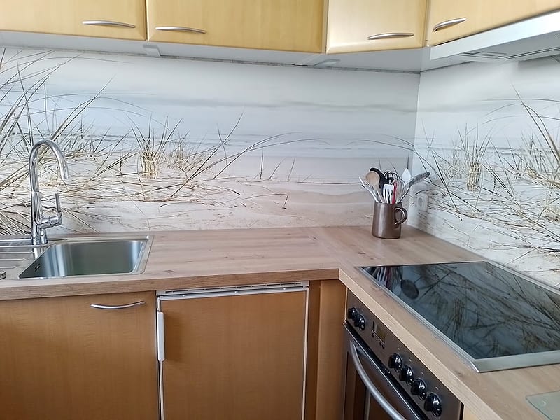 Küche im Winkel mit Spüle, Glaskeramikkochfeld, Einbaubackofen und Dünenmotiv als Rückwand