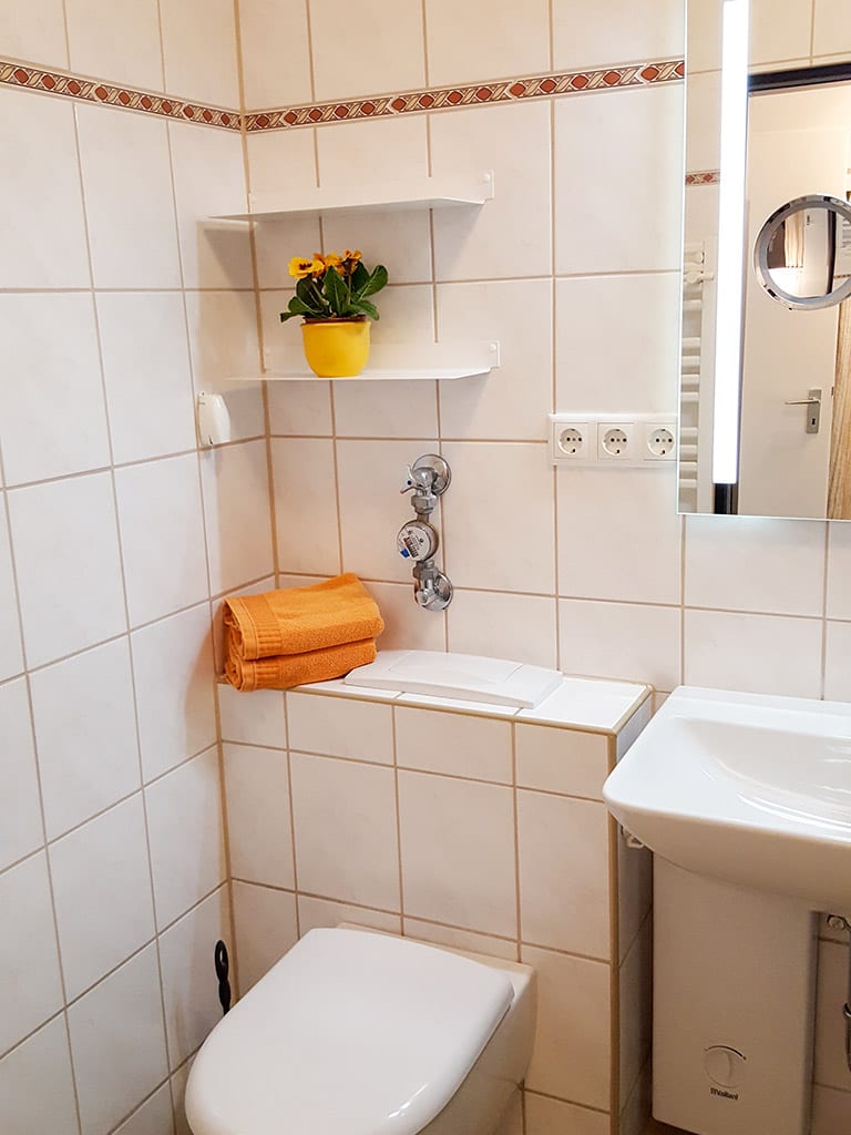 Bad mit WC, Wandregal, Handtüchern und Spiegel über dem Waschbecken