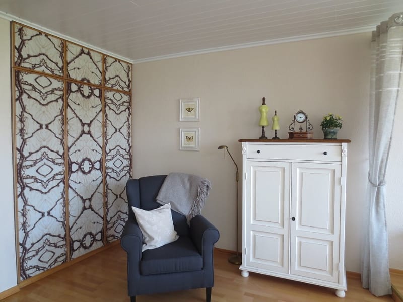 Sitzecke mit blauem Ohrensessel, weißem Schrank und gemusterter Wandfläche unter weißer Holzpaneeldecke